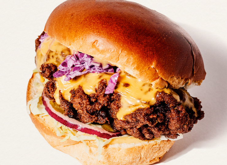 Gooey cheese and crispy chicken burger in a bun, served on a wooden board