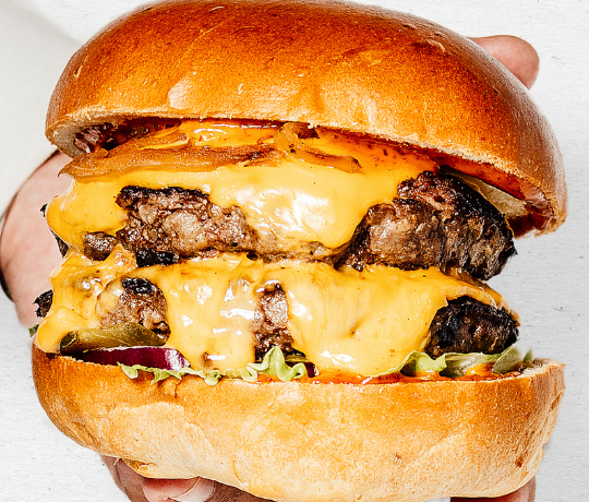 Close up of a beef burger filled with melking cheese, sauce and salad